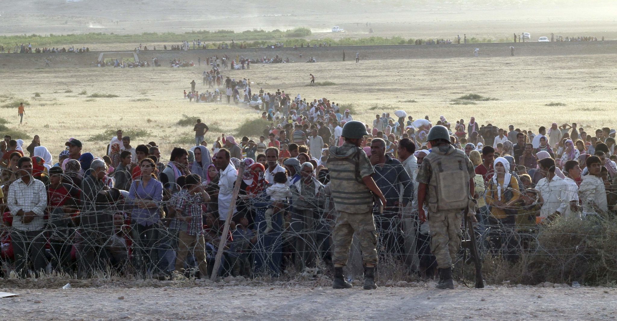 Turkish soldiers stand guard as Syrians wait behind the border fences near the southeastern town of Suruc in Sanliurfa province